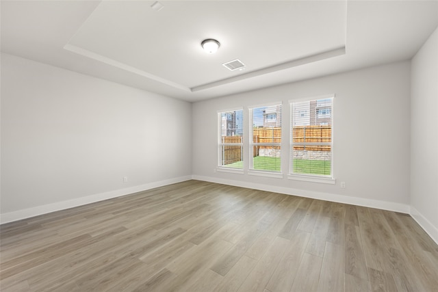 spare room with light wood-type flooring and a tray ceiling