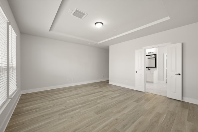 unfurnished bedroom with multiple windows, light hardwood / wood-style floors, and a tray ceiling