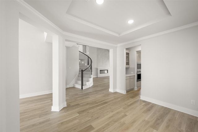 unfurnished living room with ornamental molding, a tray ceiling, and light hardwood / wood-style floors