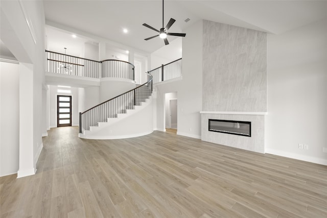 unfurnished living room with light wood-type flooring, a large fireplace, ceiling fan, and high vaulted ceiling