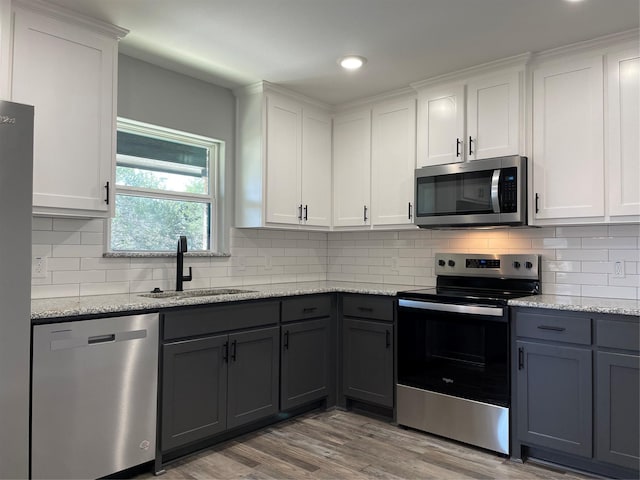 kitchen featuring appliances with stainless steel finishes, gray cabinets, light wood-type flooring, white cabinetry, and a sink