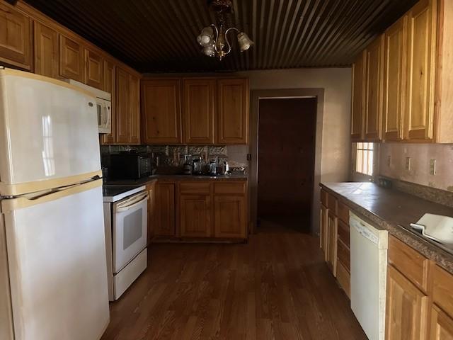 kitchen with backsplash, a notable chandelier, white appliances, and dark wood-type flooring