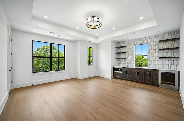 3306 Floral Mews, Frisco, TX 75033 - unfurnished living room with wine cooler, a raised ceiling, recessed lighting, bar with sink, and light wood finished floors