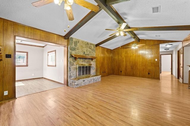 unfurnished living room featuring ceiling fan, light hardwood / wood-style flooring, lofted ceiling with beams, a textured ceiling, and a fireplace