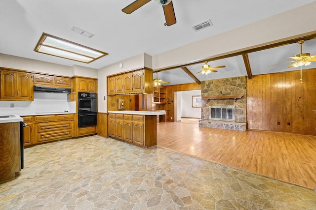 kitchen with ceiling fan, kitchen peninsula, stovetop, wooden walls, and a fireplace