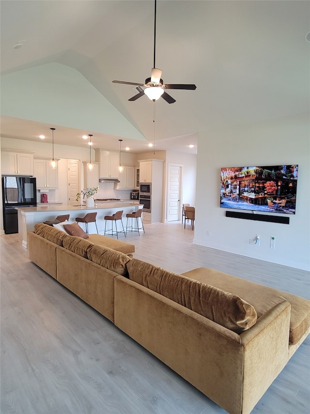 living room with ceiling fan, light wood-type flooring, and high vaulted ceiling