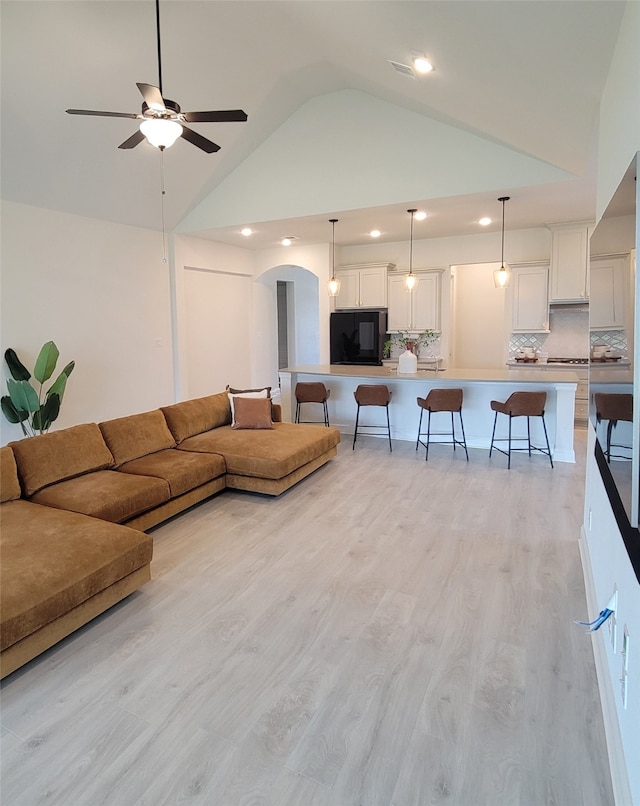 living room with ceiling fan, light wood-type flooring, and high vaulted ceiling