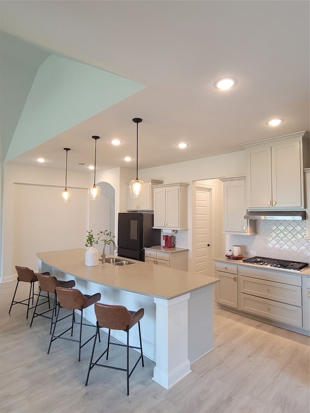 kitchen featuring sink, backsplash, light hardwood / wood-style flooring, and a center island with sink