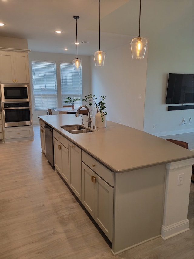 kitchen with appliances with stainless steel finishes, light hardwood / wood-style floors, sink, a kitchen island with sink, and hanging light fixtures