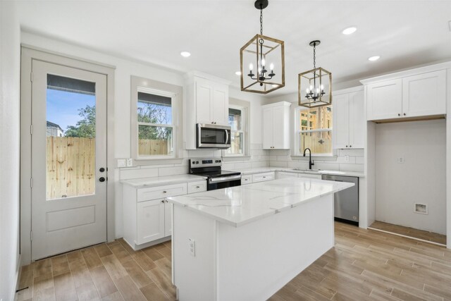 kitchen with stainless steel appliances, hanging light fixtures, light hardwood / wood-style floors, decorative backsplash, and white cabinetry