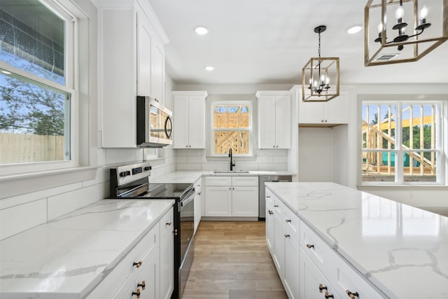 kitchen with light hardwood / wood-style flooring, a wealth of natural light, light stone counters, and stainless steel appliances