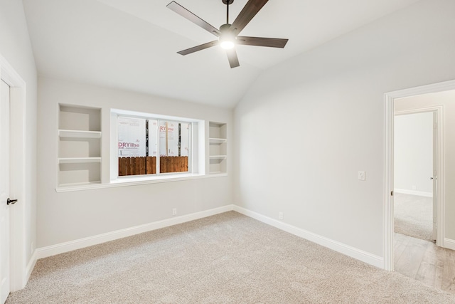 carpeted spare room featuring built in shelves, vaulted ceiling, and ceiling fan