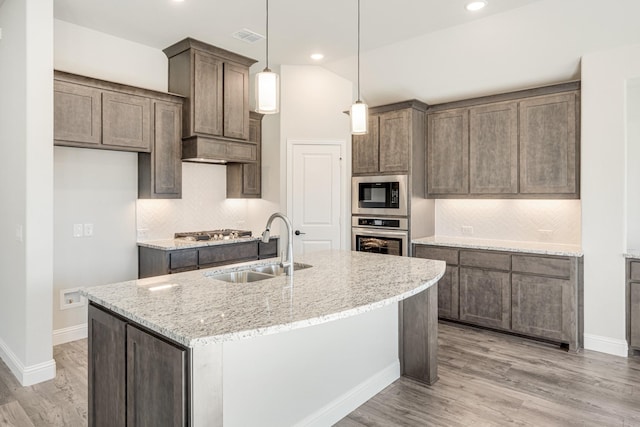 kitchen featuring sink, a kitchen island with sink, stainless steel appliances, light stone counters, and decorative light fixtures