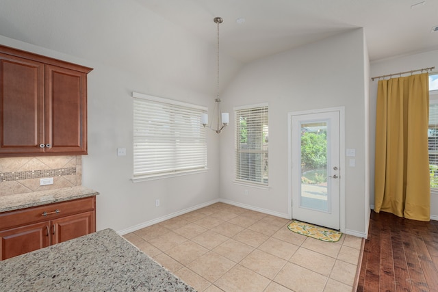 kitchen featuring light hardwood / wood-style flooring, tasteful backsplash, vaulted ceiling, pendant lighting, and light stone countertops