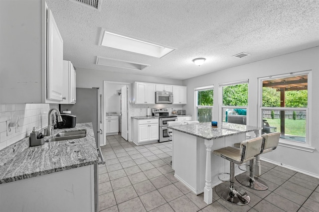 kitchen featuring white cabinetry, tasteful backsplash, light tile patterned floors, a center island, and stainless steel appliances