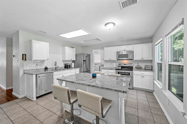 kitchen featuring white cabinets, stainless steel appliances, a center island, and light tile patterned floors