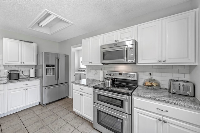 kitchen with light tile patterned flooring, separate washer and dryer, white cabinetry, tasteful backsplash, and appliances with stainless steel finishes