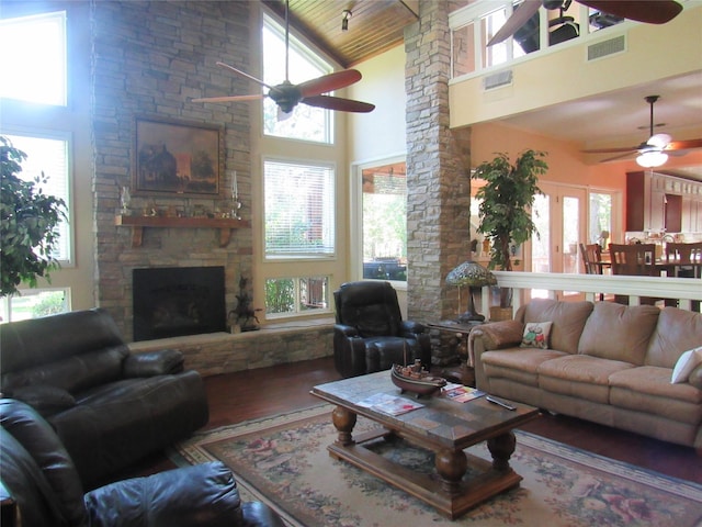 living area featuring visible vents, a towering ceiling, a ceiling fan, a stone fireplace, and wood finished floors