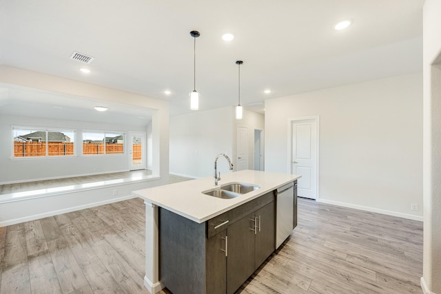 kitchen featuring dishwasher, sink, dark brown cabinetry, light hardwood / wood-style floors, and a center island with sink