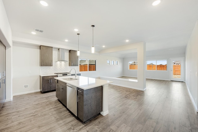 kitchen featuring wall chimney exhaust hood, sink, hanging light fixtures, dishwasher, and a kitchen island with sink