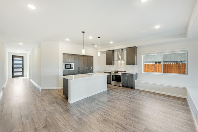 kitchen with sink, appliances with stainless steel finishes, hanging light fixtures, a center island with sink, and wall chimney exhaust hood