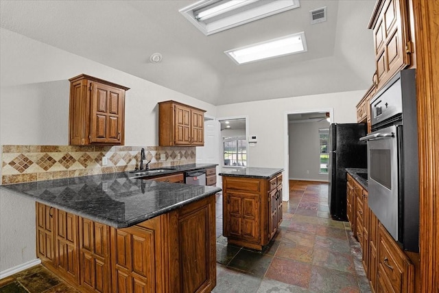 kitchen with appliances with stainless steel finishes, sink, dark stone countertops, backsplash, and kitchen peninsula