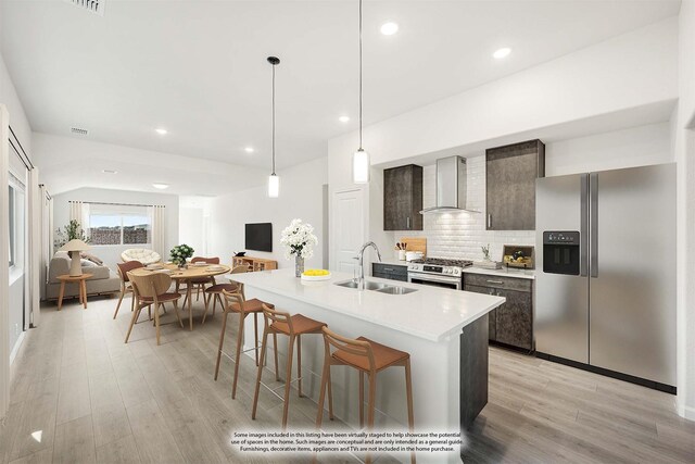 kitchen featuring wall chimney range hood, sink, a kitchen island with sink, black microwave, and stainless steel gas range oven