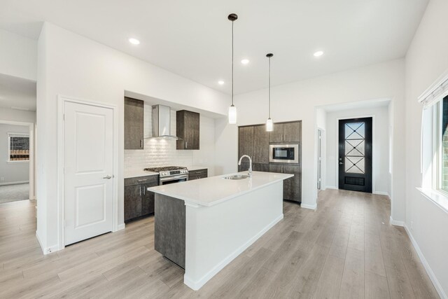 kitchen with sink, a kitchen island with sink, stainless steel dishwasher, dark brown cabinetry, and light hardwood / wood-style floors