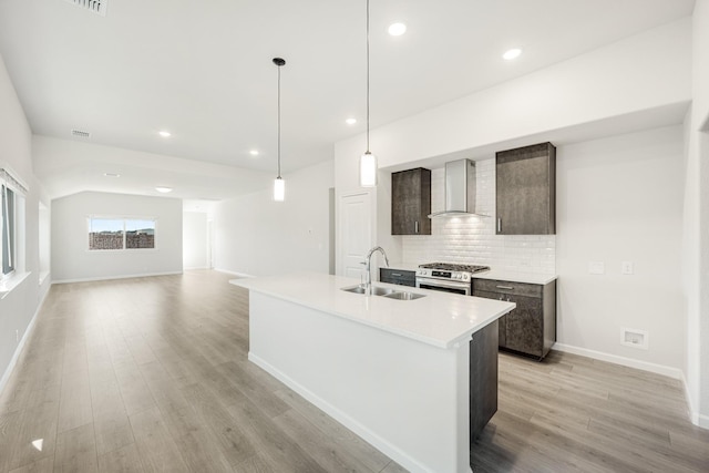 kitchen with dark brown cabinetry, sink, gas range, a center island with sink, and wall chimney range hood