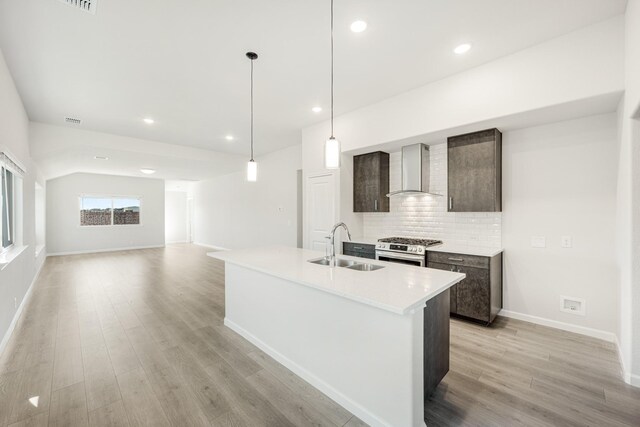 kitchen with hanging light fixtures, sink, a center island with sink, and wall chimney exhaust hood