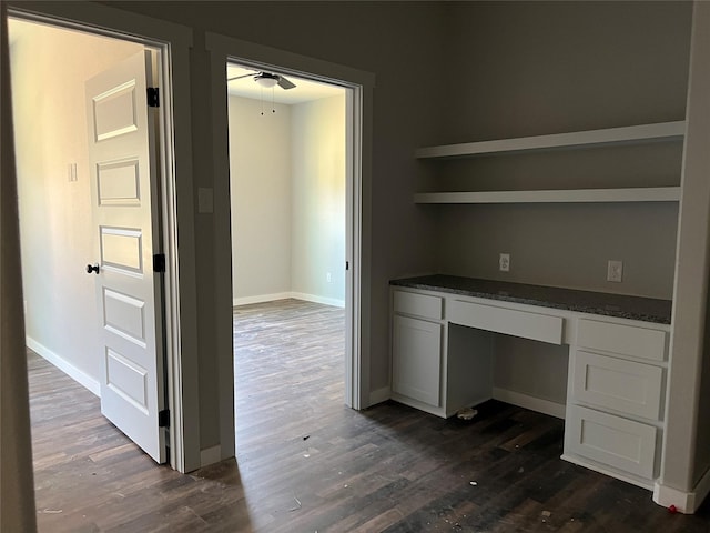 unfurnished office featuring dark wood-type flooring, built in desk, and ceiling fan