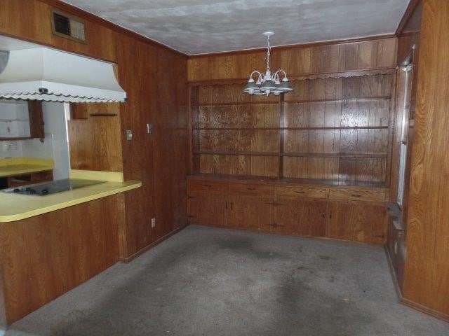 kitchen featuring wood walls, black electric stovetop, light colored carpet, and a chandelier