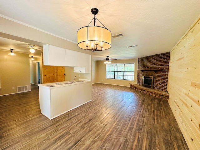 unfurnished living room featuring crown molding, ceiling fan with notable chandelier, wood walls, a brick fireplace, and hardwood / wood-style flooring