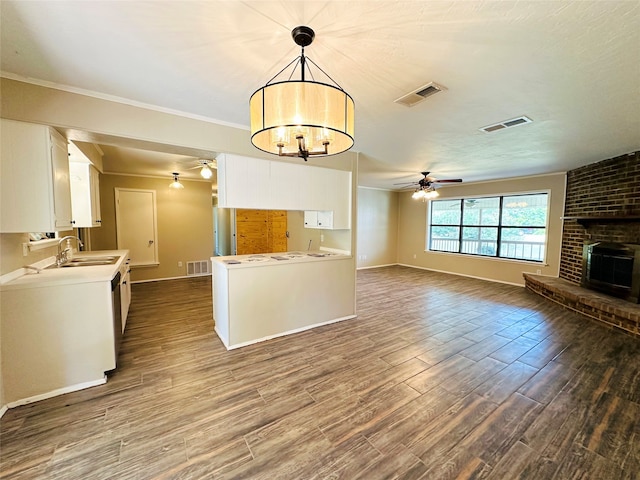 kitchen featuring wood-type flooring, ceiling fan with notable chandelier, pendant lighting, ornamental molding, and a brick fireplace