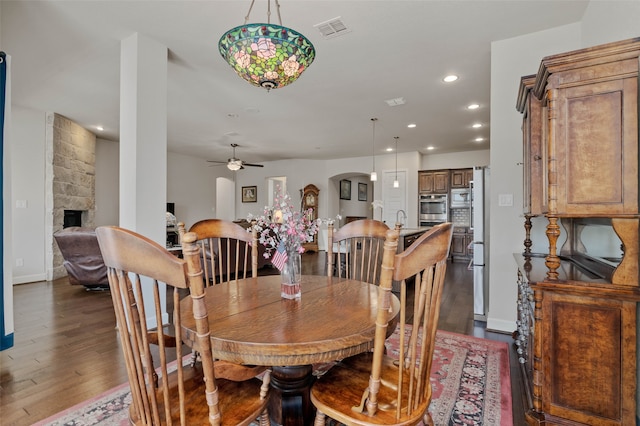 dining area with a fireplace, ceiling fan, and dark hardwood / wood-style flooring