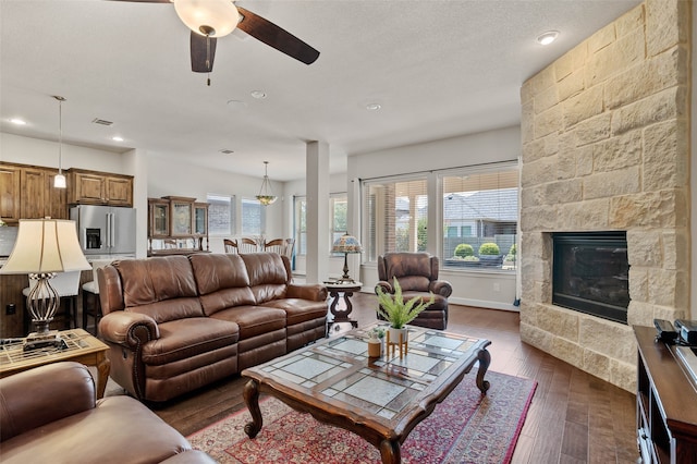 living room featuring a textured ceiling, ceiling fan, dark wood-type flooring, and a stone fireplace