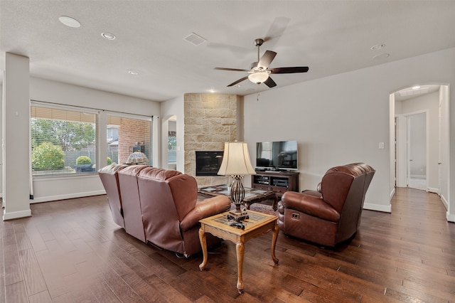 living room featuring a stone fireplace, ceiling fan, and dark hardwood / wood-style flooring