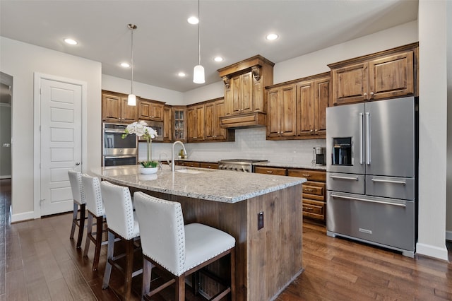 kitchen featuring dark hardwood / wood-style flooring, a center island with sink, stainless steel appliances, and decorative light fixtures