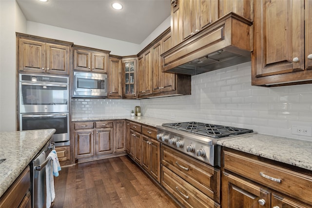 kitchen featuring stainless steel appliances, tasteful backsplash, light stone counters, dark hardwood / wood-style flooring, and custom exhaust hood