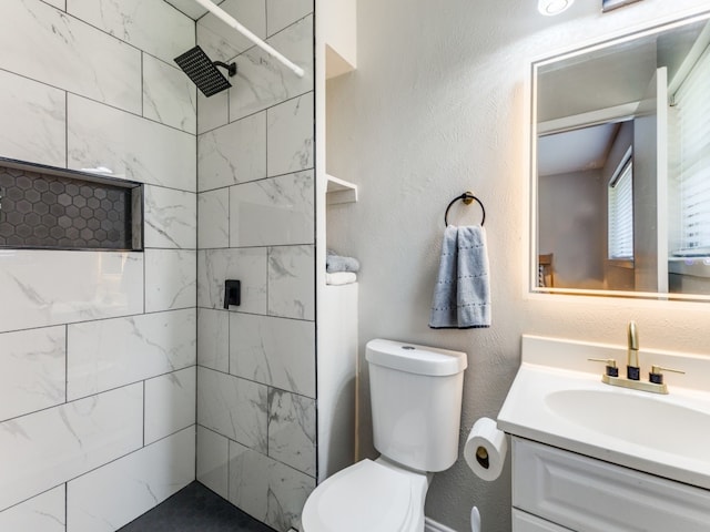 bathroom featuring toilet, a tile shower, and vanity