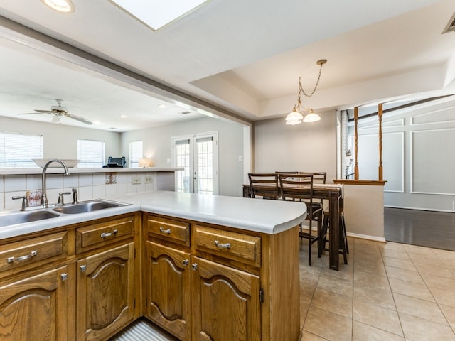 kitchen with ceiling fan with notable chandelier, light tile patterned floors, kitchen peninsula, sink, and hanging light fixtures