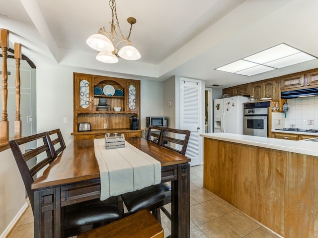 tiled dining space with a raised ceiling and a chandelier