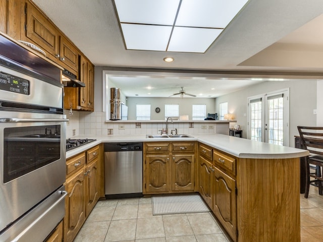 kitchen with stainless steel appliances, kitchen peninsula, sink, decorative backsplash, and light tile patterned flooring