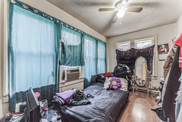 bedroom featuring multiple windows, hardwood / wood-style floors, a textured ceiling, and cooling unit