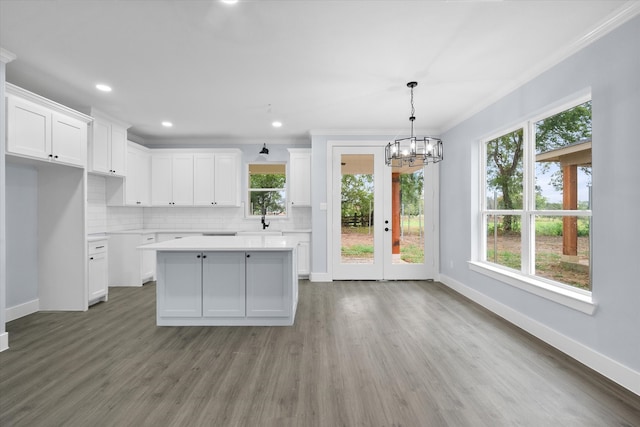 kitchen featuring pendant lighting, ornamental molding, a kitchen island, white cabinetry, and hardwood / wood-style floors