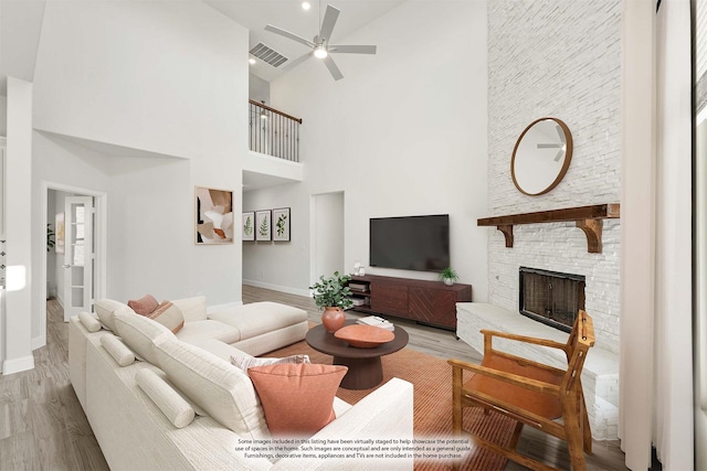 living room with ceiling fan, a fireplace, light hardwood / wood-style floors, and a high ceiling