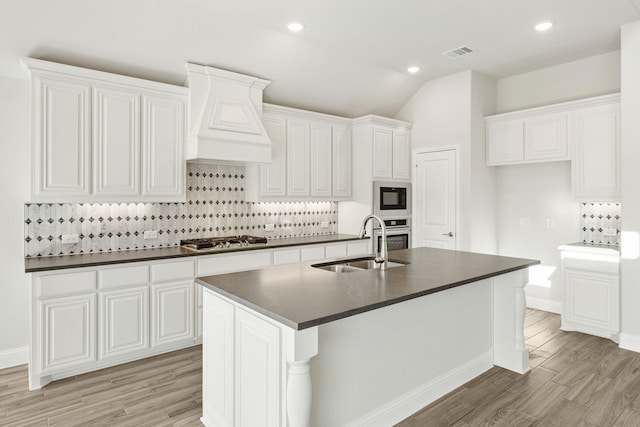 kitchen featuring sink, custom exhaust hood, white cabinetry, stainless steel appliances, and a kitchen island with sink