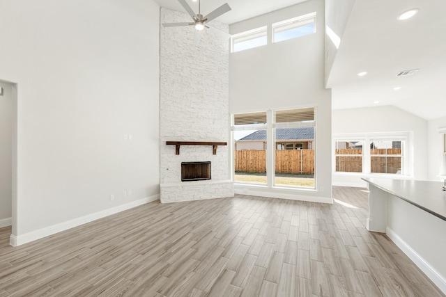 unfurnished living room featuring a high ceiling, a stone fireplace, ceiling fan, and light hardwood / wood-style flooring