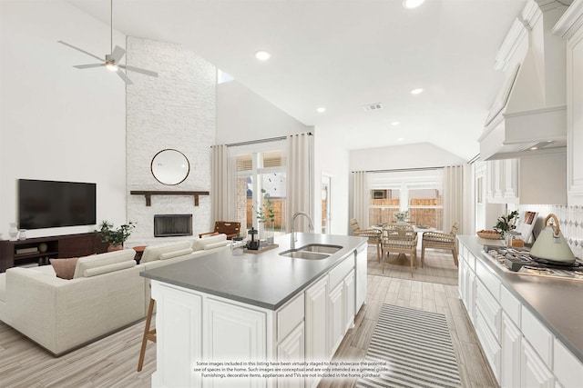 kitchen with stainless steel gas stovetop, an island with sink, sink, white cabinets, and plenty of natural light