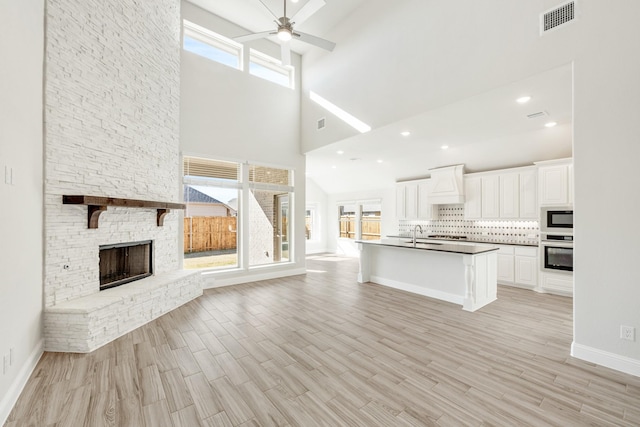 kitchen featuring premium range hood, white cabinets, built in microwave, a stone fireplace, and oven